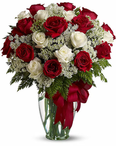 Bouquet of red and white roses in a clear vase with a red bow on a white background