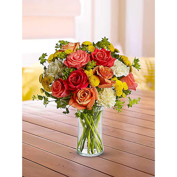 Red, orange, and yellow flower bunch in clear vase on wooden tabel