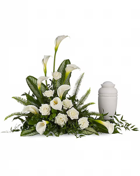 Fresh white floral bouquet with green leaves alongside white urn on white surface