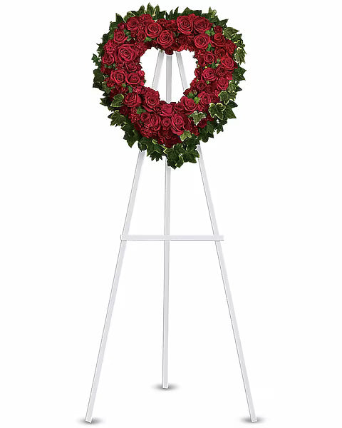 Heart-shaped wreath of red roses on a white stand
