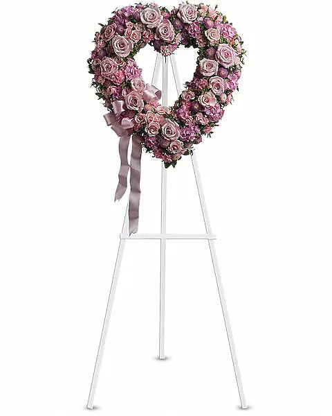 Heart-shaped floral arrangement with pink and purple flowers on a white stand against a white background