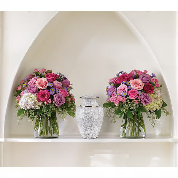 Two bouquets of flowers and a decorative vase on a white shelf.