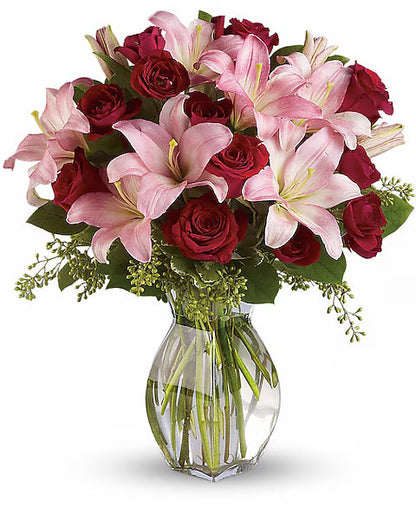 Bouquet of pink lilies and red roses in a clear vase on a white background