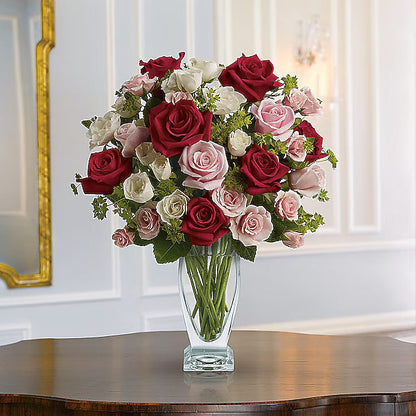 Red, white, and pink roses arranged in vase on tabletop.