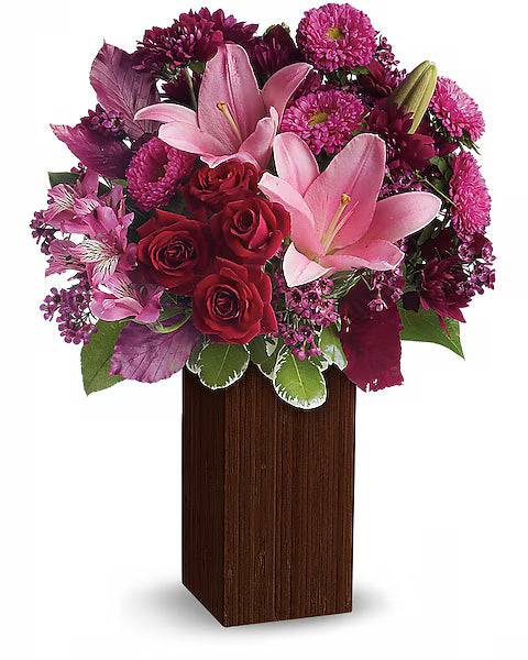 Bouquet of pink lilies, red roses, and purple flowers in a wooden vase on a white background