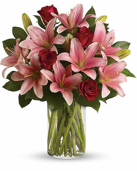 Bouquet of pink lilies and red roses in a clear vase on a white background